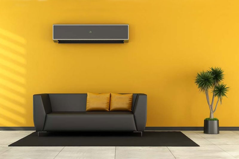 Custom design ductless mini split mounted on yellow wall with couch underneath.