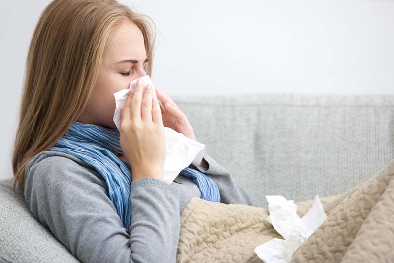 Close up of a young woman sneezing into a tissue.|Close up of a young woman sneezing into a tissue.