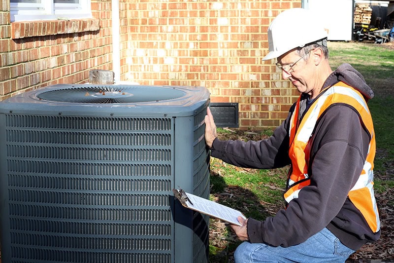5 Reasons Why Regular HVAC Maintenance is Essential Homeowners. Photo of a technician inspecting an HVAC Unit installed outside of a home or building.