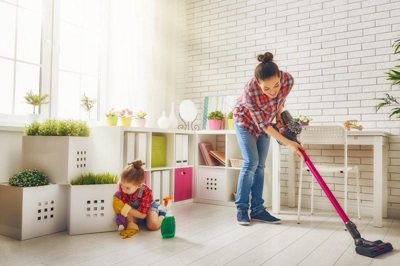 Mother and daughter do the cleaning in the house. A young woman and a little child girl wiped the dust and vacuumed the floor.