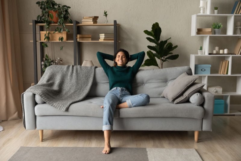 A man on the couch with arms overhear relaxing.